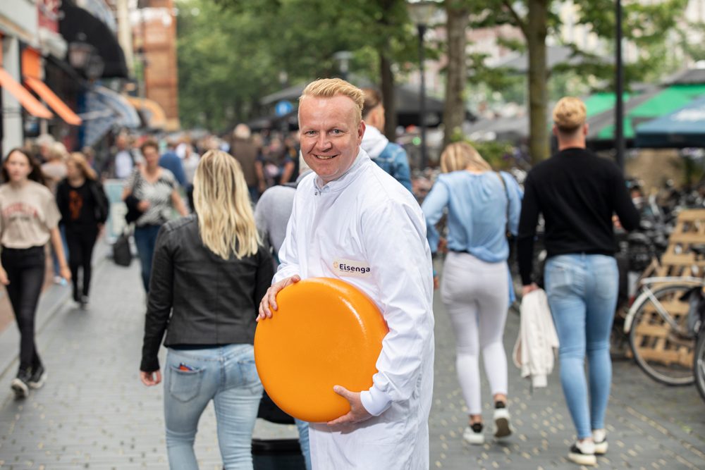 Medewerker van Kaasvoordeelshop met een kaaswiel in de winkelstraat